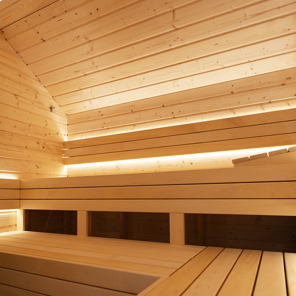 LED Illuminated Indoor Residential Finnish Sauna Interior of a wooden sauna with tiered benches and soft backlit lighting.